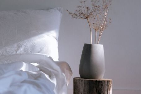 Bed Linen - A White Bed with Linen Near the Chopped Wood with Ceramic Vase on Top