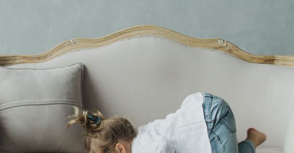 Sofa - Side view full body adorable little girl in casual clothes lying on cozy comfortable sofa with face down against blue wall on daylight
