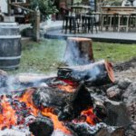 Build A Fire Pit - Stone fire pit with burning firewood placed on courtyard of residential building with chairs and table on terrace in countryside