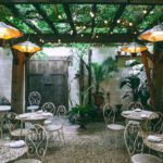 Patio Furniture Material - Cafe with setting on ornamental tables near chairs under decorative lamps in backyard on summer day